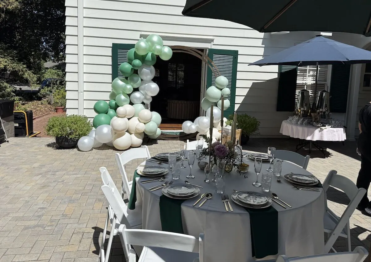 Sage and ivory balloon garland over a doorway paired with a bloom-accented tablescape — balloon and floral styling for Vallejo catering parties