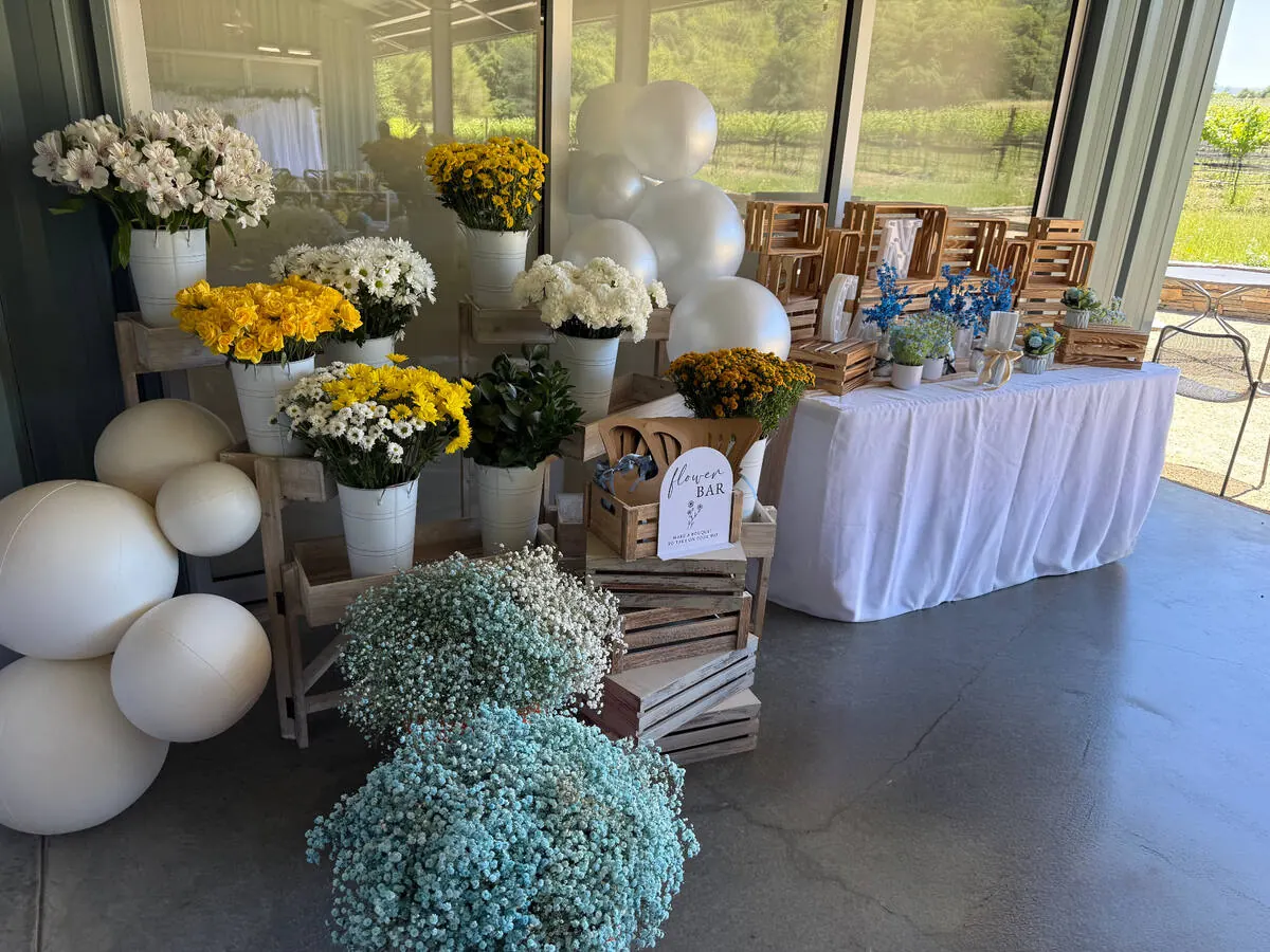 Bloom bar stocked with yellow roses, daisies and baby's breath alongside ribbon and paper for guests to wrap bouquets — bloom bar experience from Napa catering
