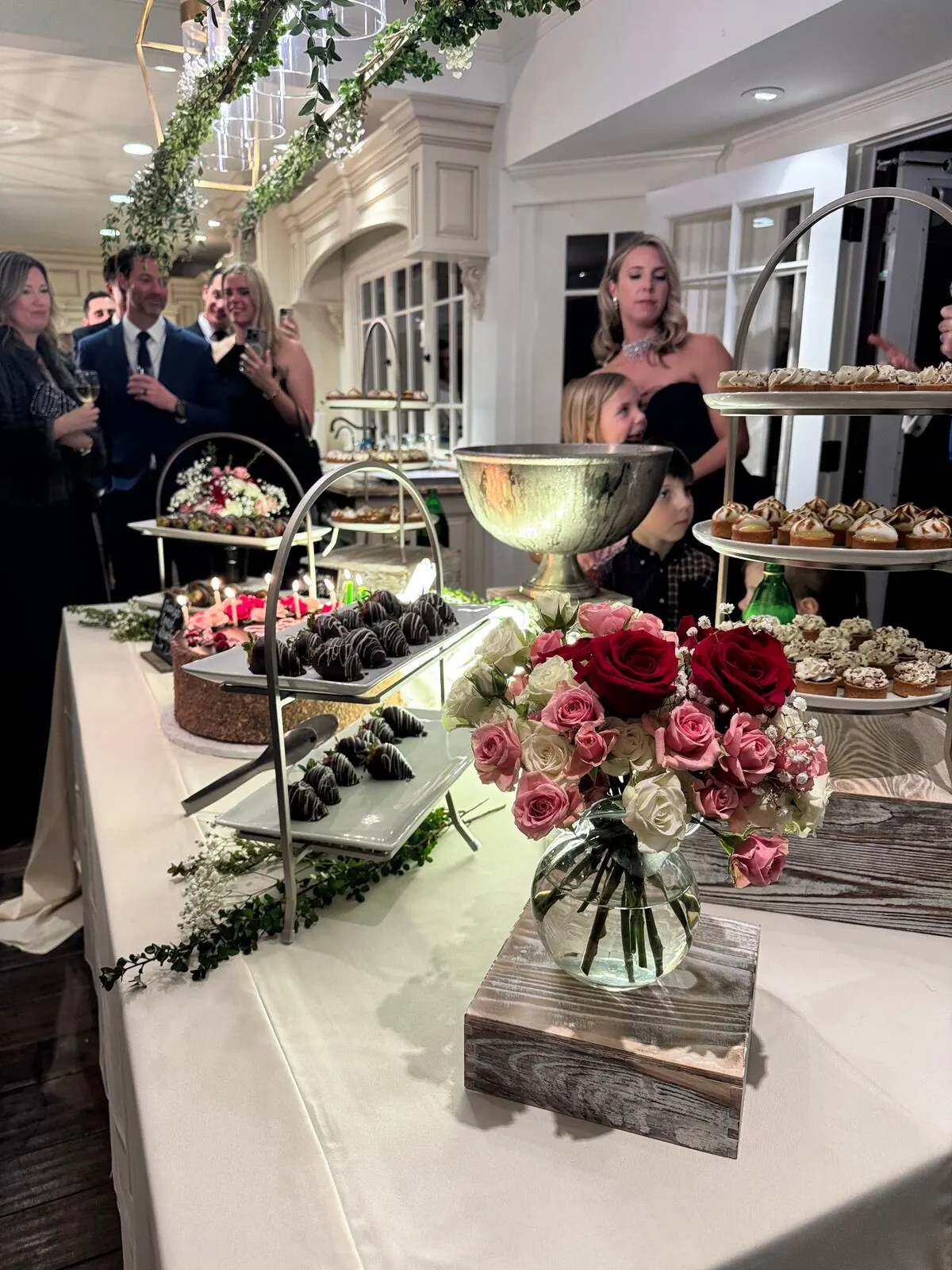 Reception sweets table with garden roses set between chocolate-dipped strawberries and petite pastries — wedding floral desserts for Napa catering